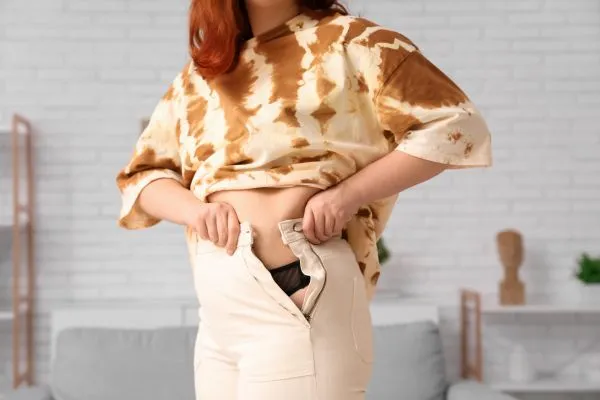 Image of woman trying to do her trousers up after pregnancy weight gain Harrow