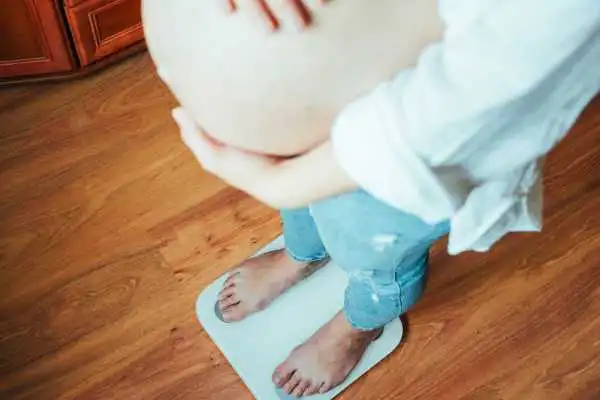 Image of woman weighing herself and experiencing weight gain through pregnancy Harrow